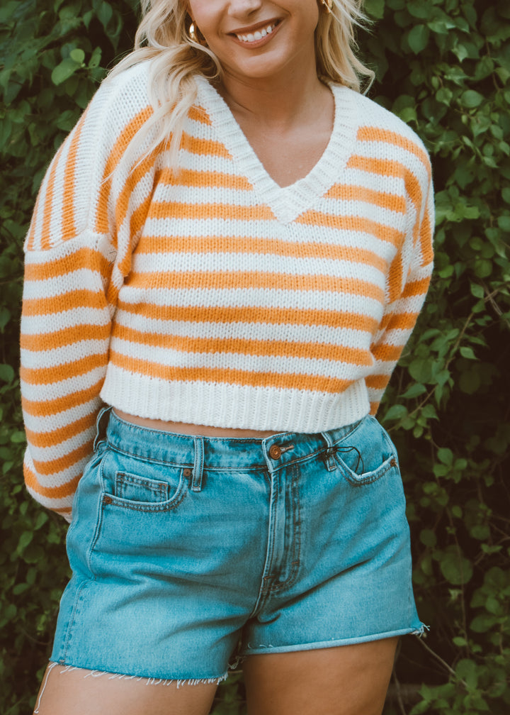 Woman wearing a striped sweater and denim shorts against a green leafy background
