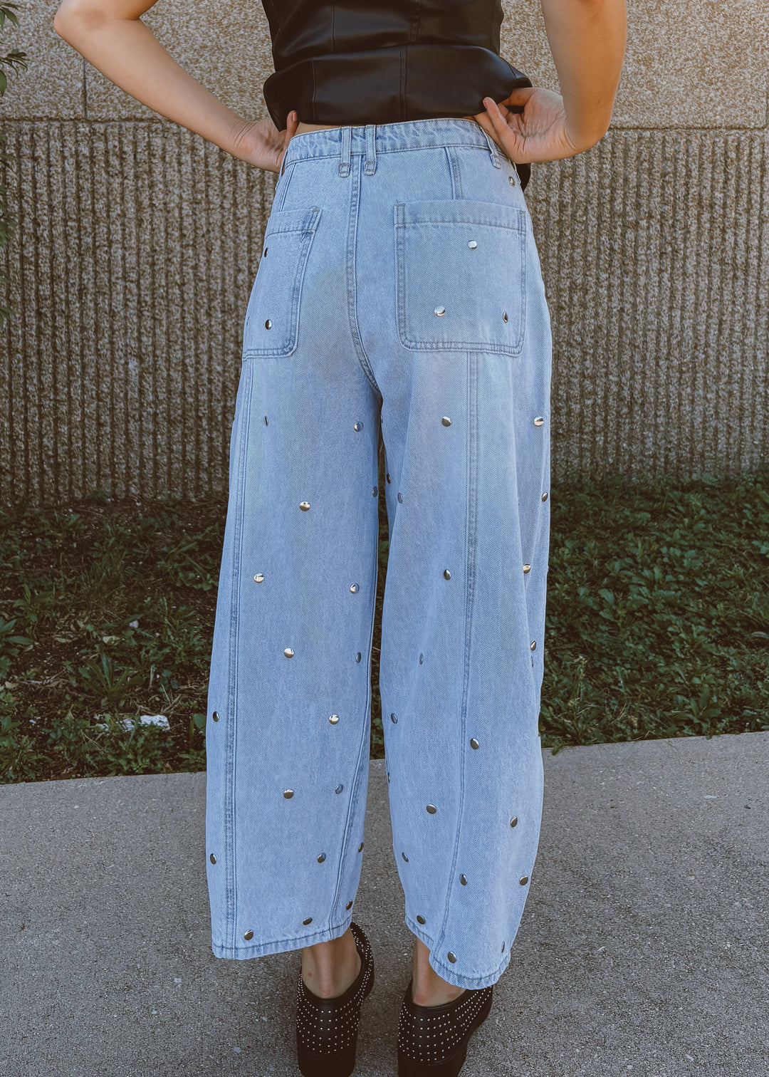 Person wearing light blue jeans with decorative studs outdoors.