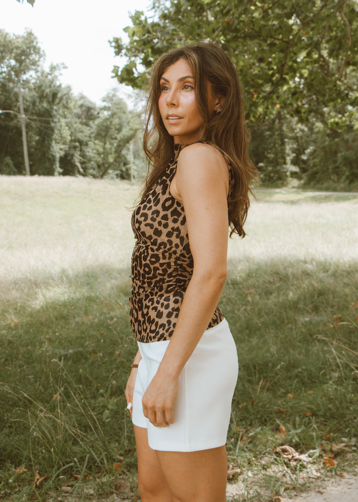 Woman wearing a leopard print top and white shorts standing in a grassy field.