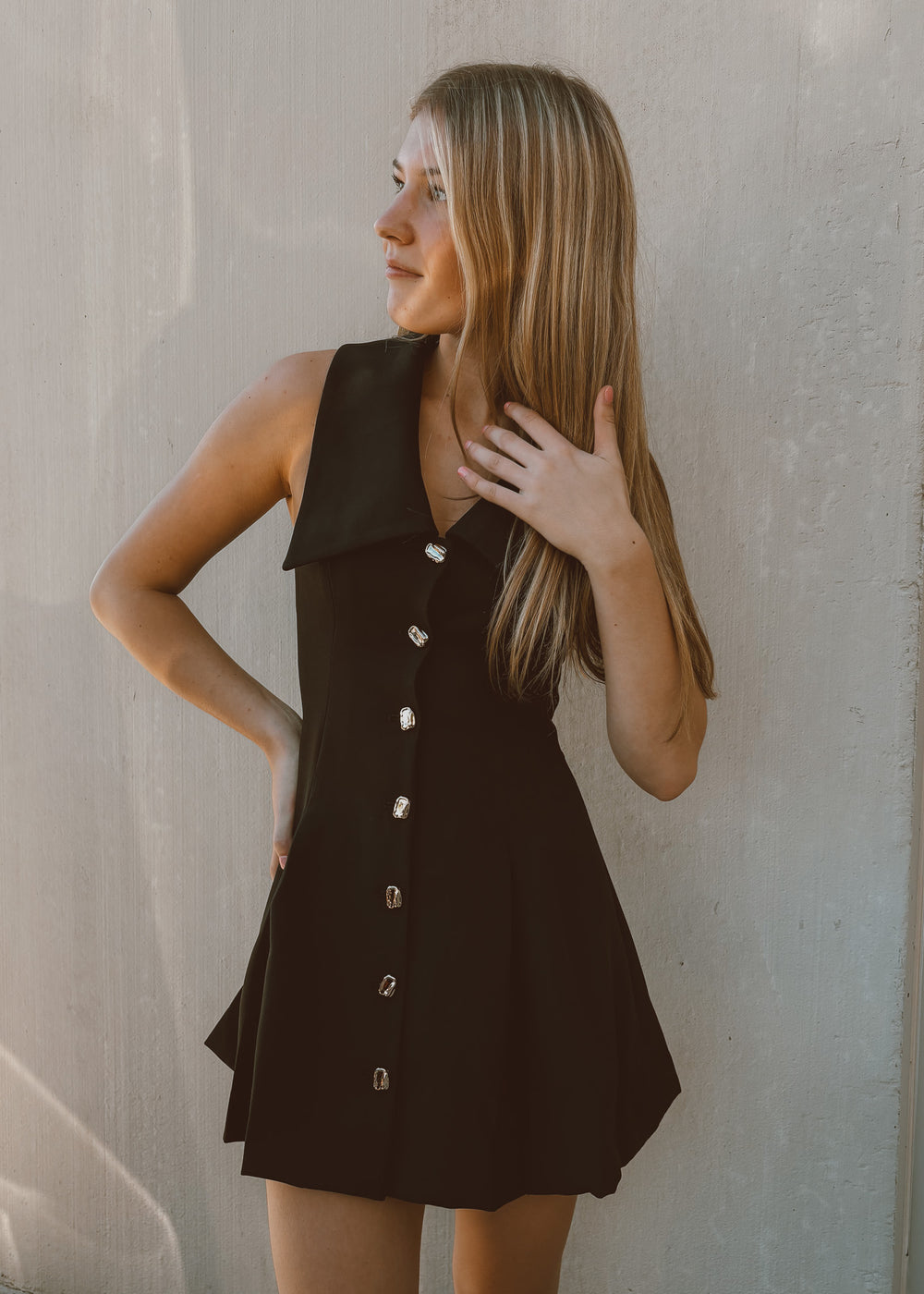 Woman wearing a black collared sleeveless dress with buttons against a plain background