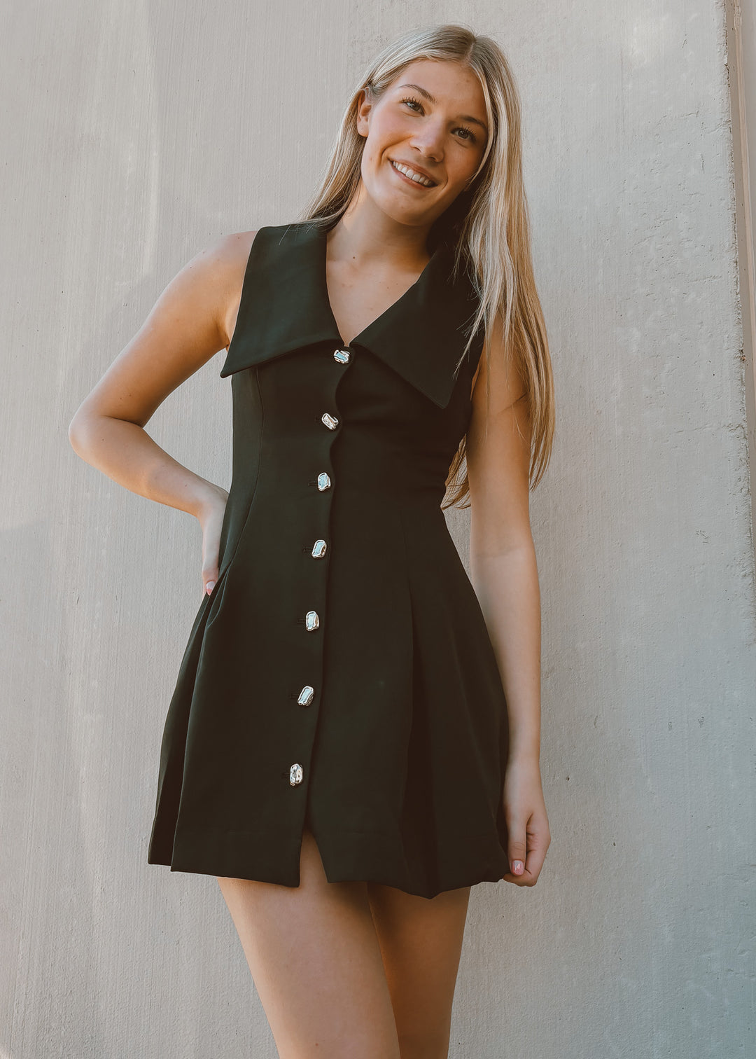 Woman wearing a black dress with gold buttons against a plain background