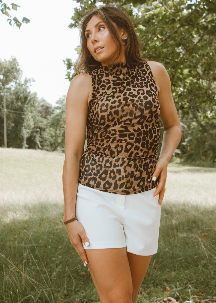Woman wearing a leopard print top and white shorts standing in a grassy field.