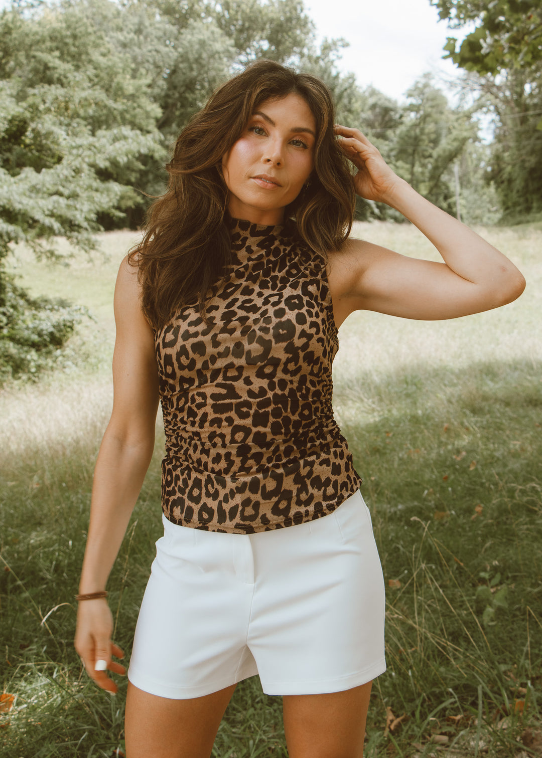 Woman wearing a leopard print top and white shorts standing in a grassy field.