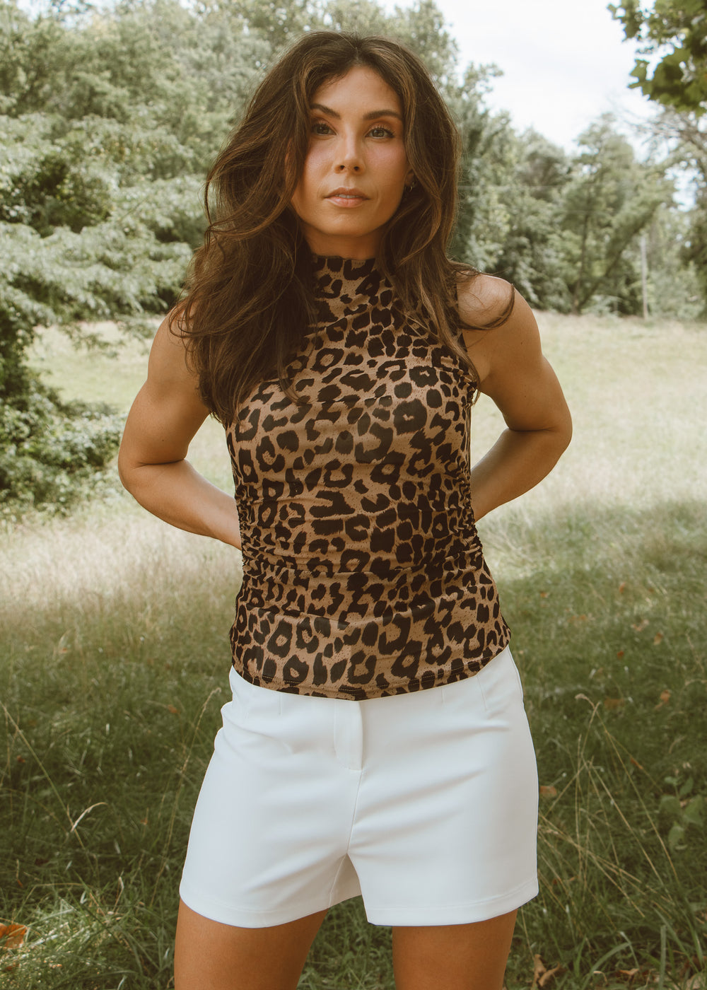 Woman wearing a leopard print top and white shorts standing in a grassy field.