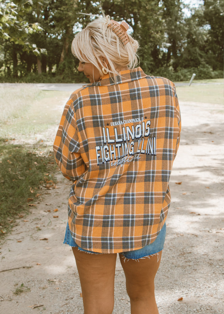 Person wearing a plaid shirt with 'Illinois Fighting Illini' text outdoors.