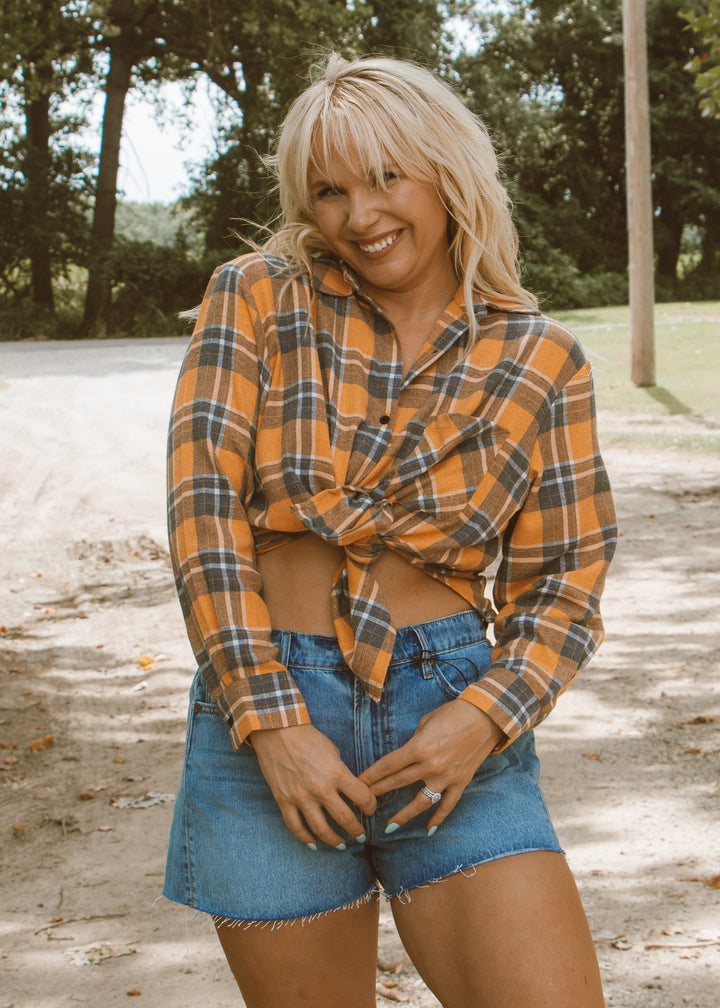 Woman wearing a plaid shirt and denim shorts standing outdoors with trees in the background