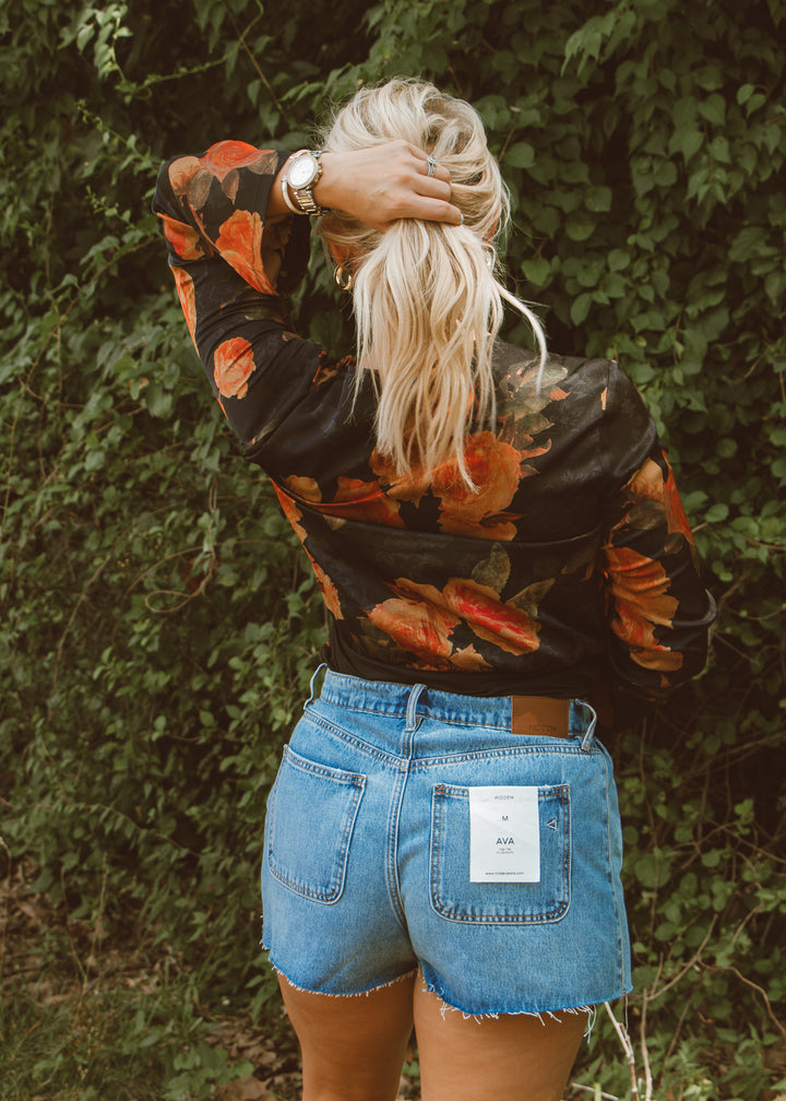 Woman wearing a floral blouse and denim shorts with a green leafy background