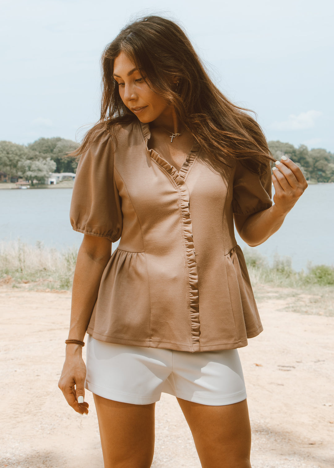 Woman wearing a brown blouse and white shorts by a lake