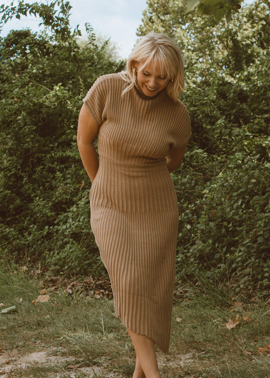 Woman wearing a ribbed knit dress standing in a natural setting with greenery.
