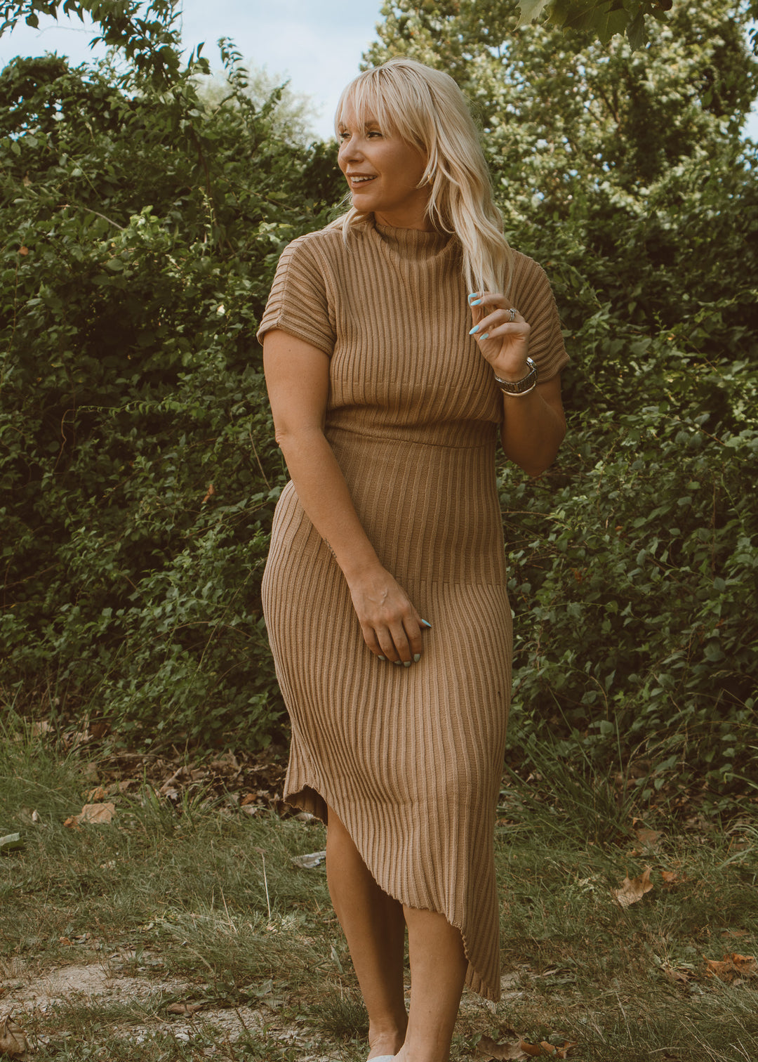 Woman in a brown ribbed dress standing outdoors with greenery in the background
