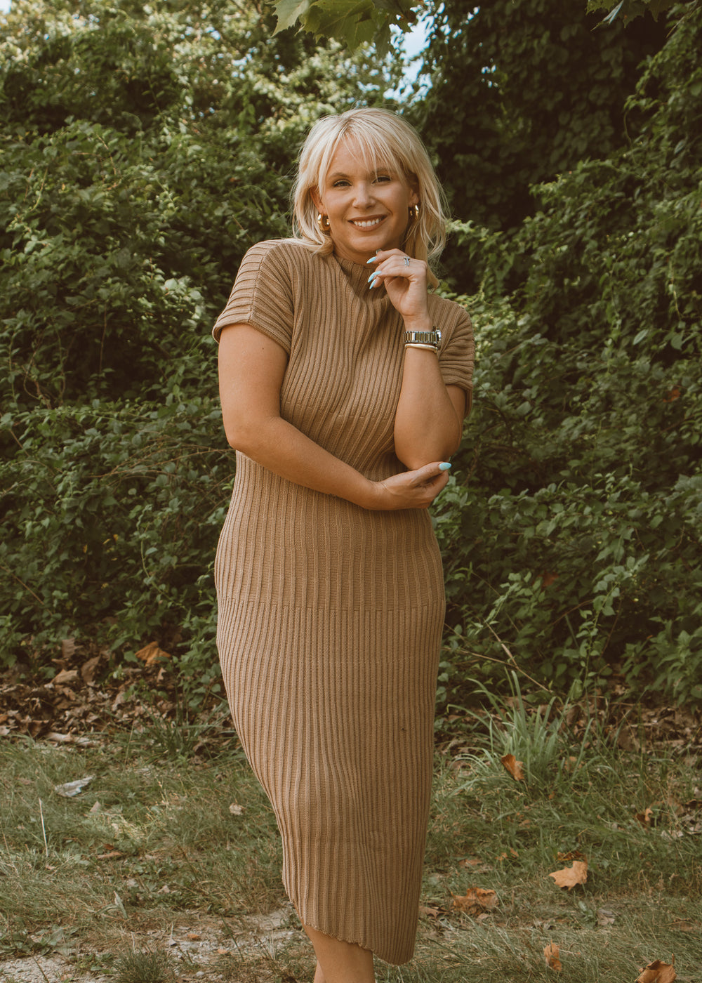 Woman in a brown ribbed dress standing outdoors with greenery in the background