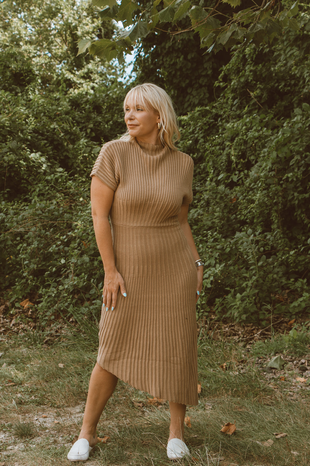 Woman in a brown ribbed dress standing in a forested area