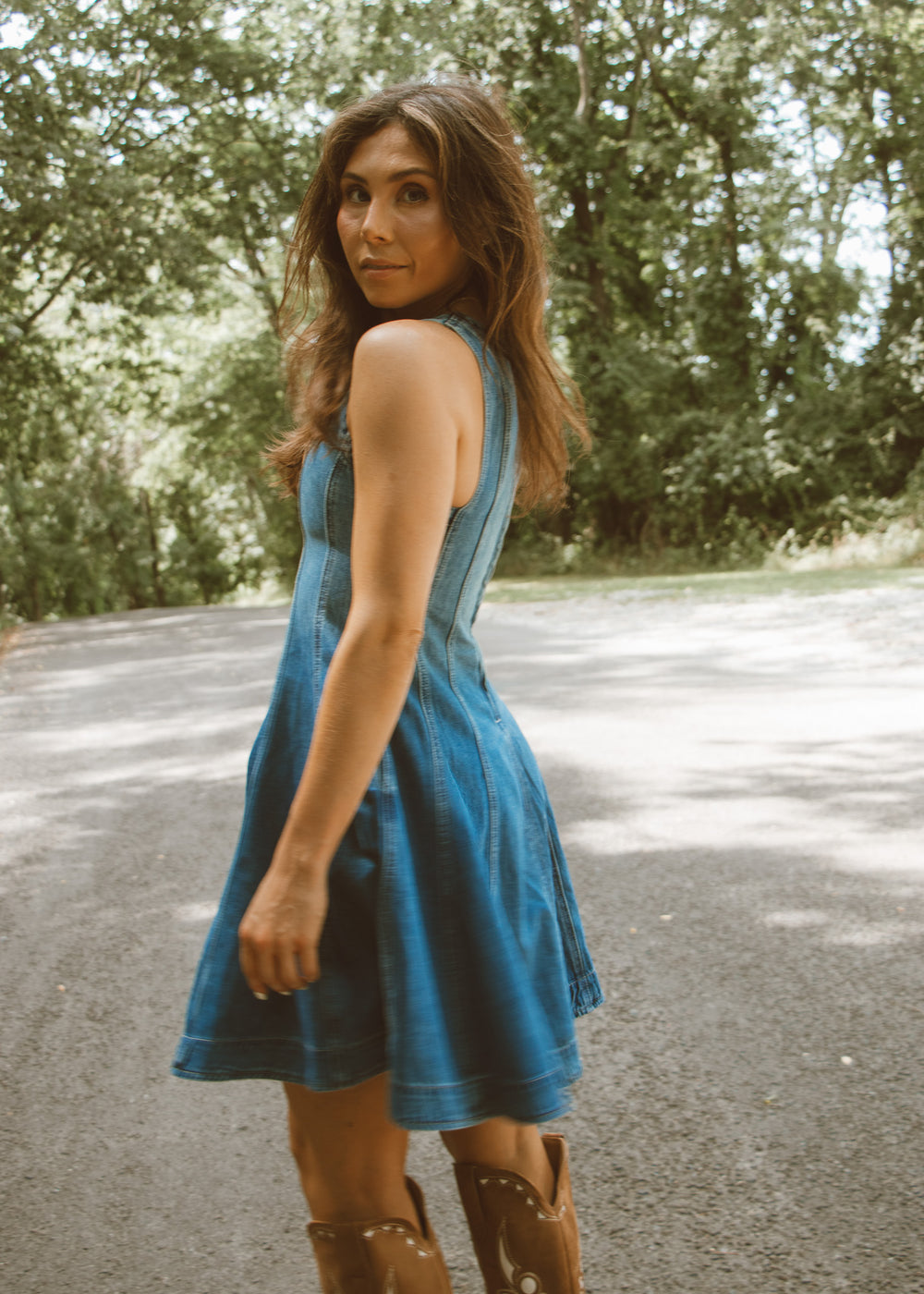 Woman in a blue dress standing on a road with trees in the background