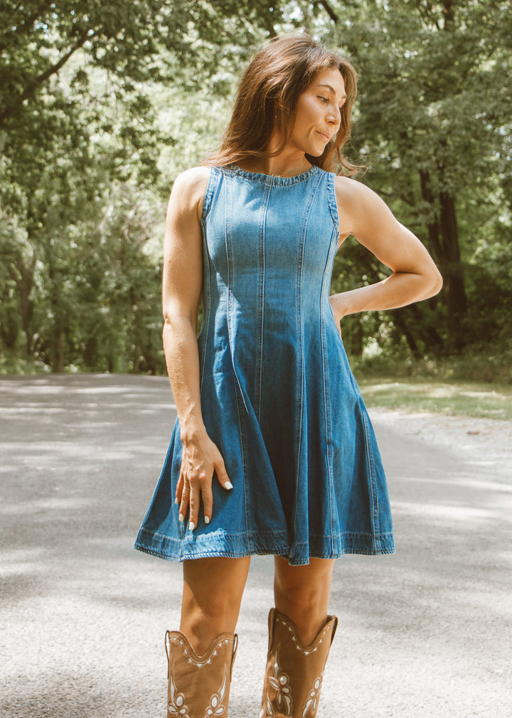 Woman wearing a blue dress and brown boots standing outdoors with trees in the background