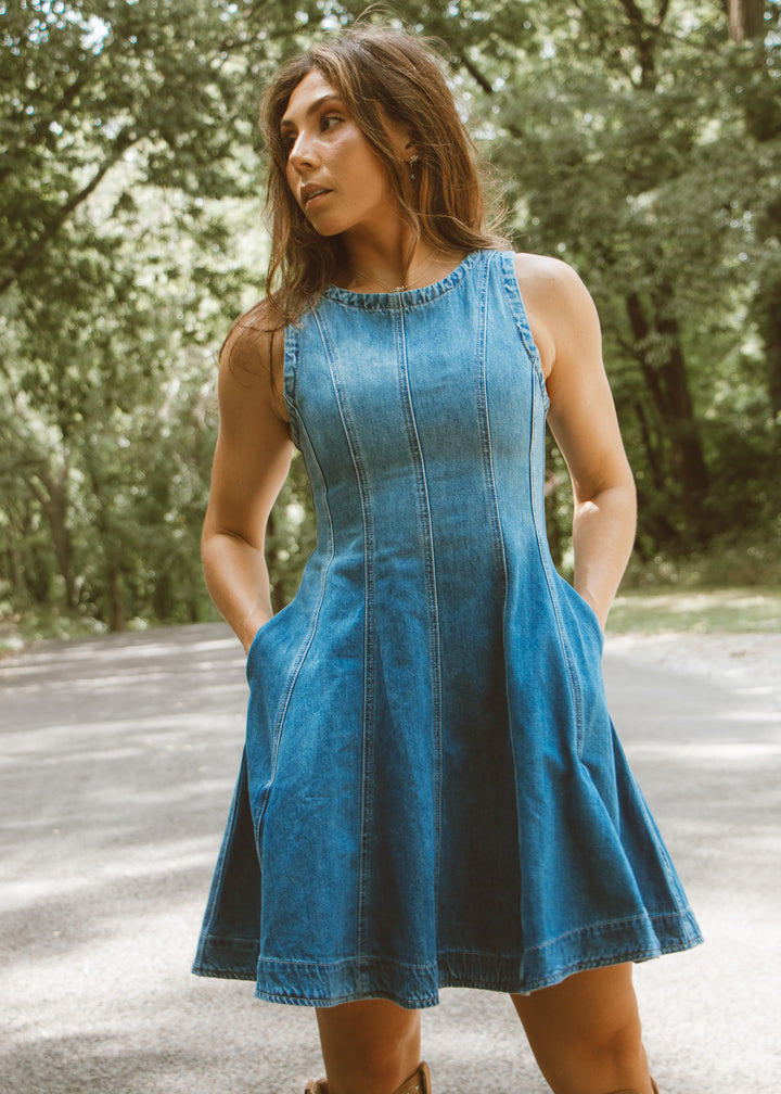 Woman wearing a blue denim dress standing outdoors with trees in the background