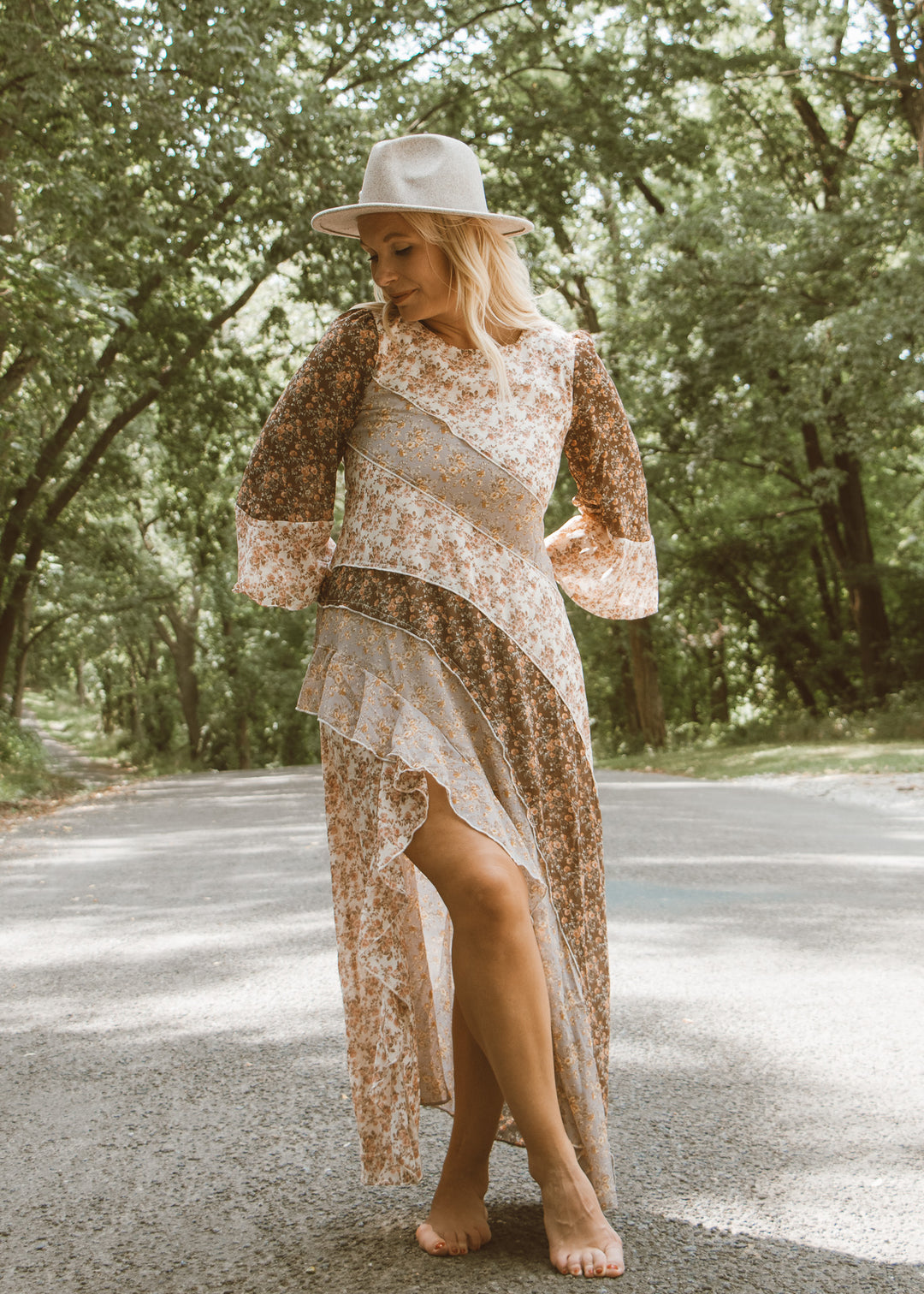 Woman in a floral dress and hat standing on a road with trees in the background