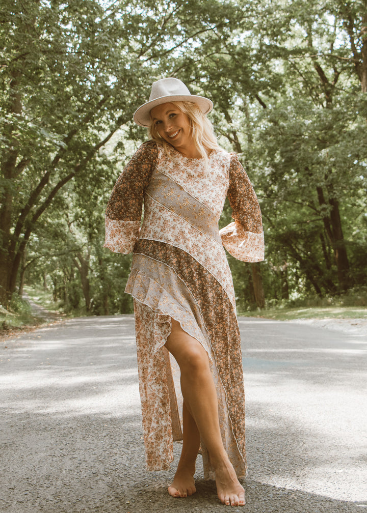 Woman in a floral dress and hat standing on a road with trees in the background