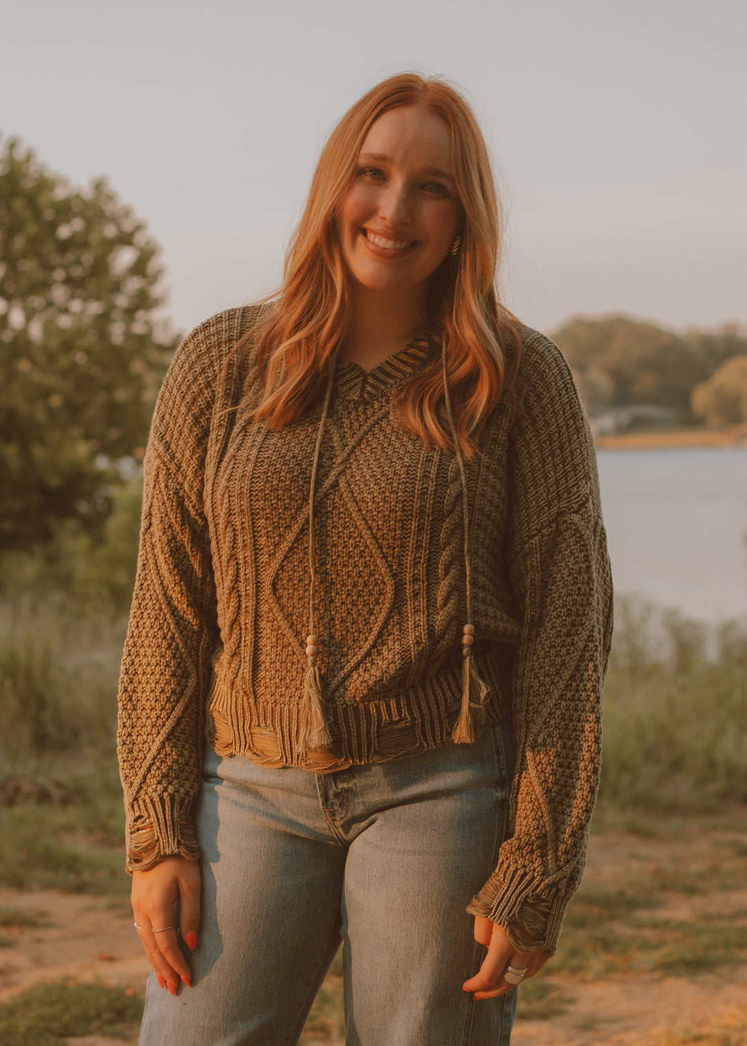 Woman wearing a green knitted sweater standing outdoors by a lake.