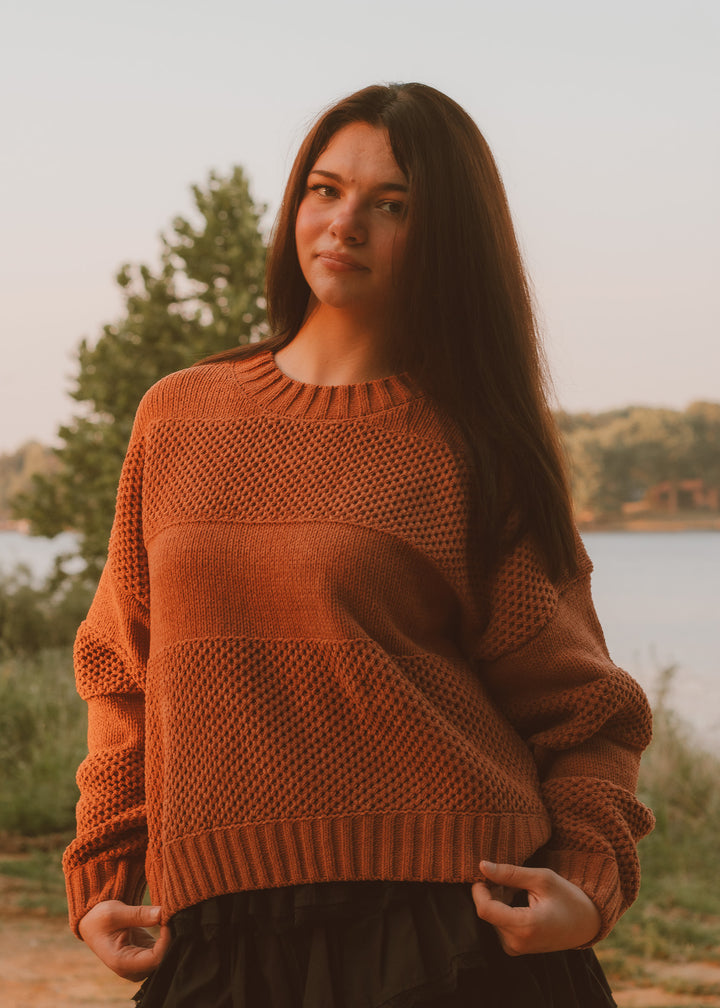 Woman wearing a brown sweater standing outdoors by a lake