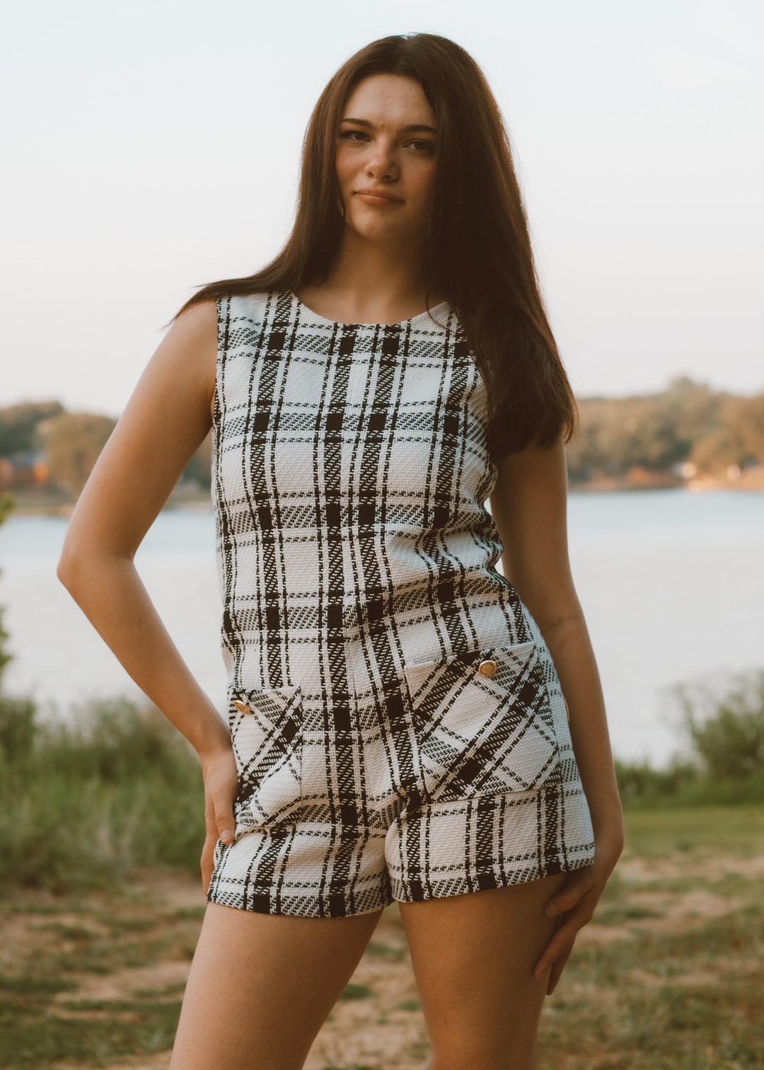 Woman wearing a plaid romper standing outdoors by a lake
