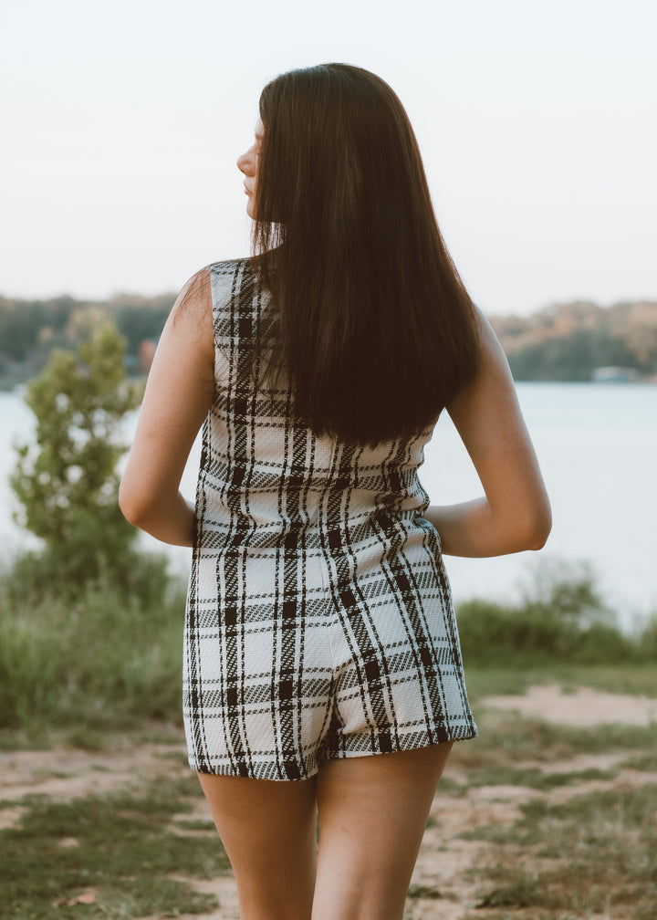 Woman in a plaid romper standing by a body of water with a blurred background
