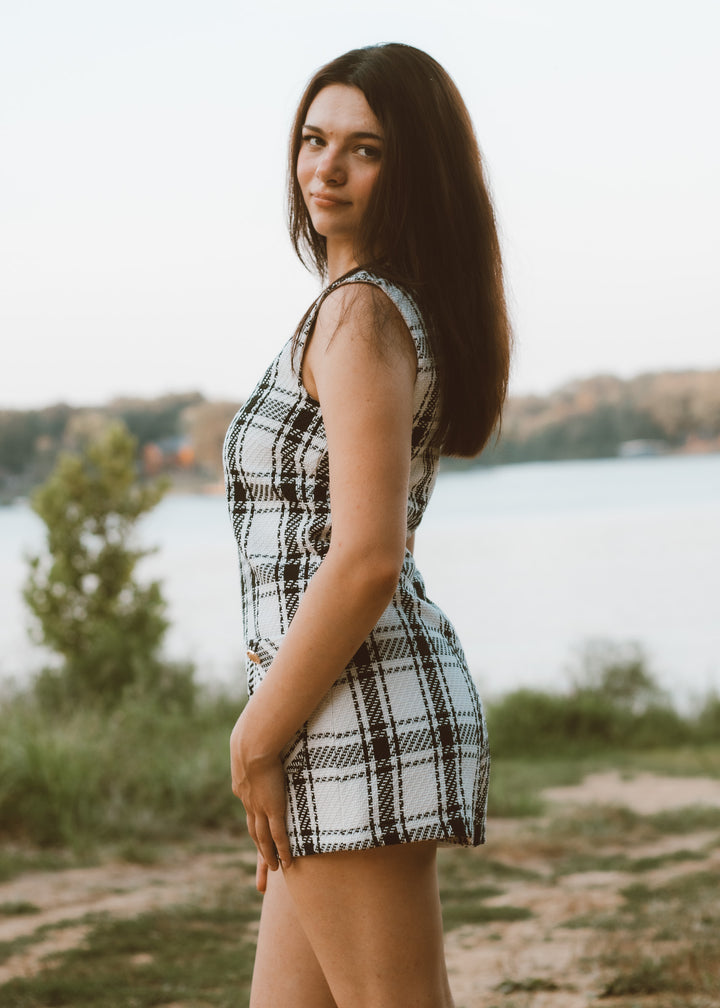 Woman in a plaid romper standing by a lake with a blurred background