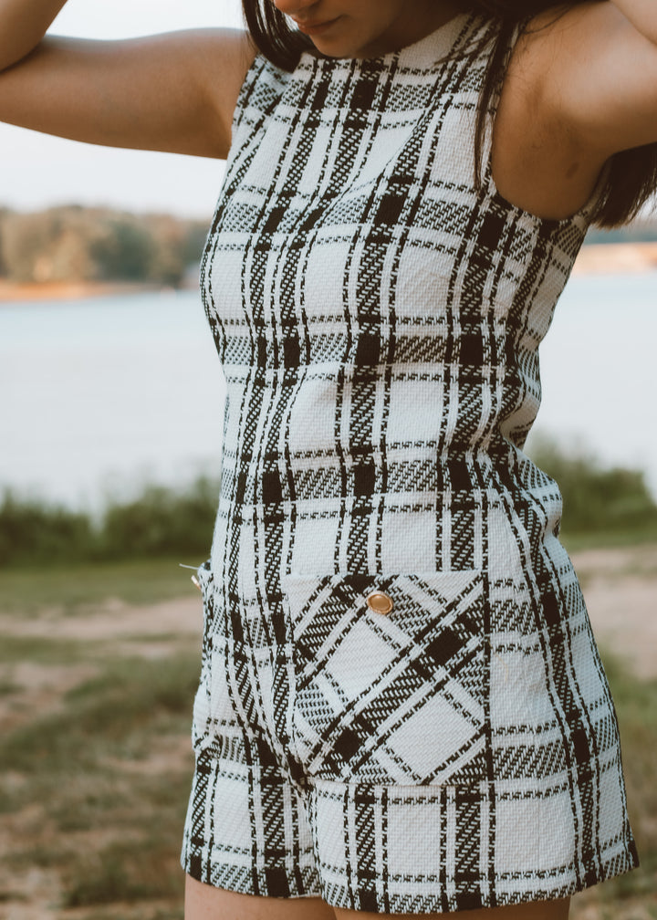 Person wearing a plaid romper with a blurred natural background