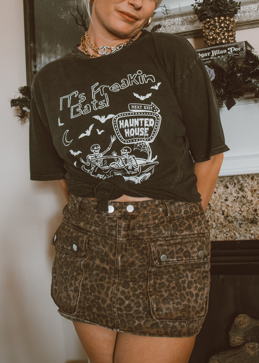 Person wearing a black t-shirt with Halloween-themed design and a leopard print skirt.