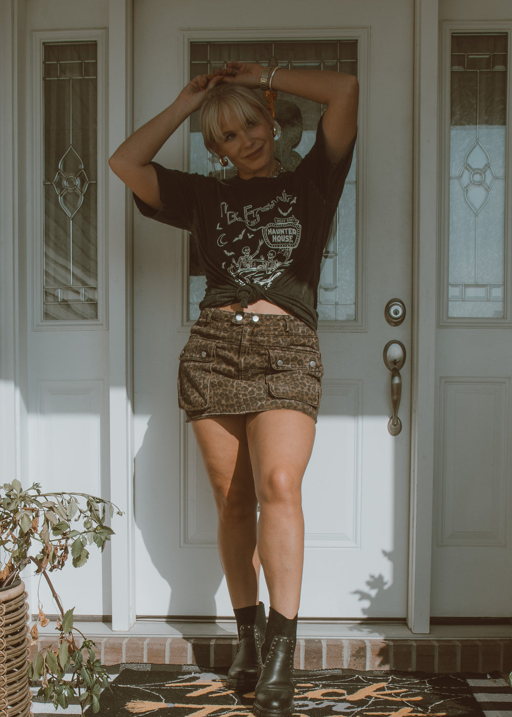 Person standing in front of a door wearing a graphic t-shirt and leopard skirt.