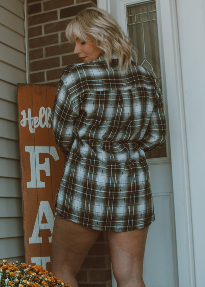 Woman wearing a plaid romper standing in front of a door.