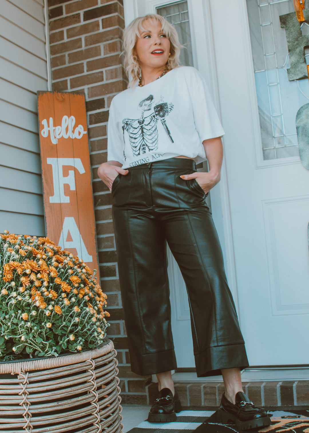 Woman standing on a porch wearing a white t-shirt and black leather pants.