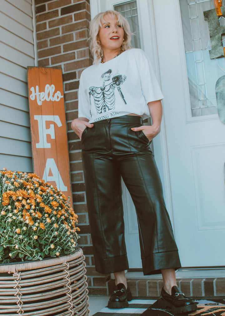 Woman standing on a porch wearing a white t-shirt and black leather pants.