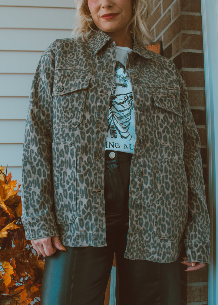 Person wearing a leopard print jacket over a graphic t-shirt, standing in front of a brick wall.