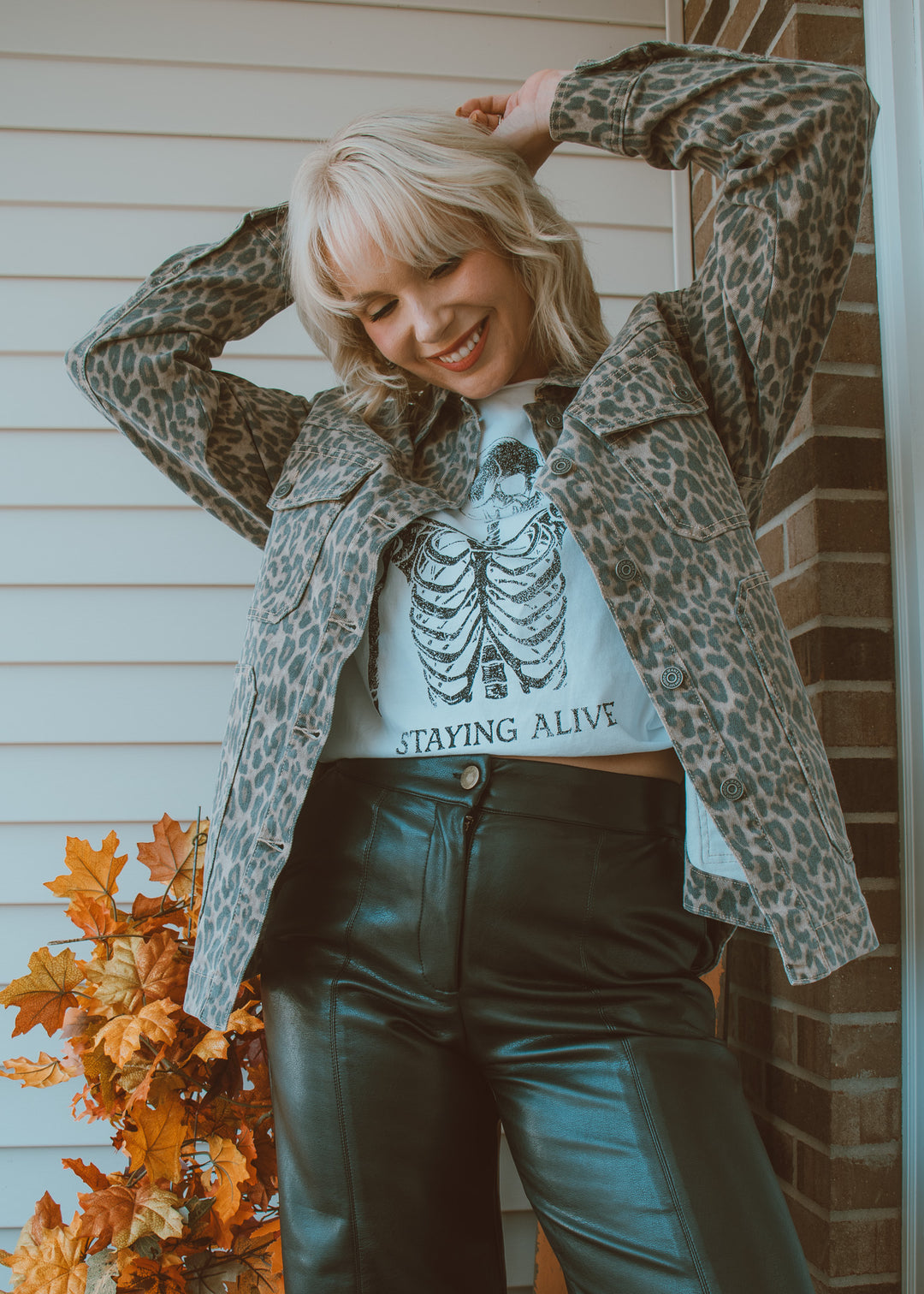 Woman wearing a leopard print jacket over a graphic t-shirt with text, standing outdoors.