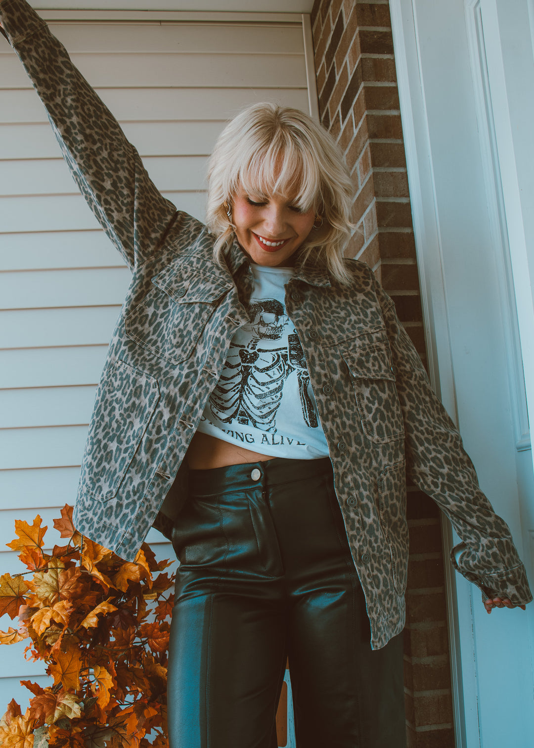 Woman wearing a leopard print jacket and black pants standing in front of a house.