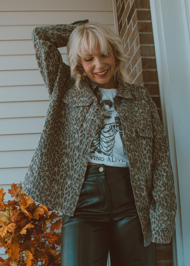 Woman wearing a leopard print jacket and black pants standing in front of a brick wall.