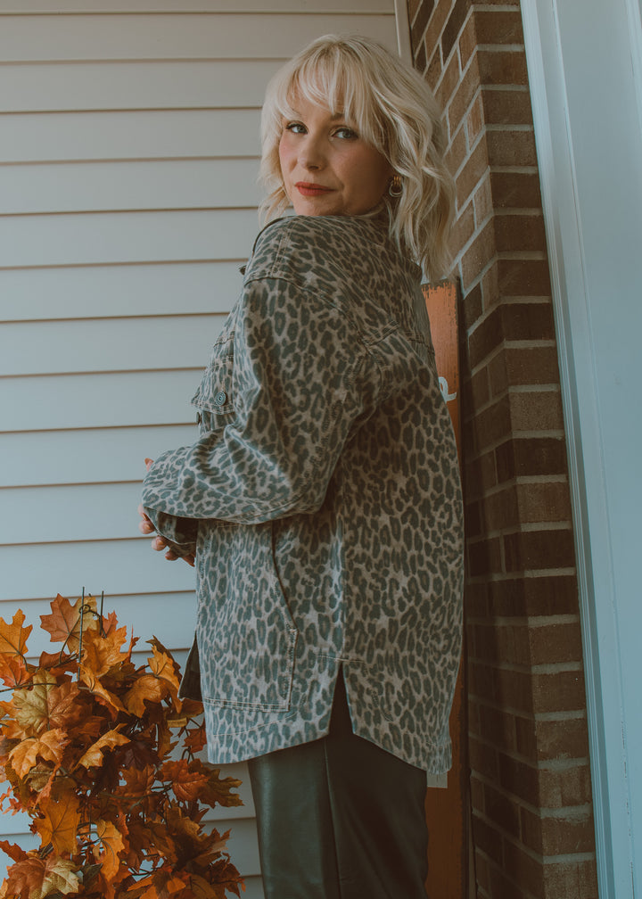 Woman wearing a leopard print jacket standing against a brick wall with autumn leaves.