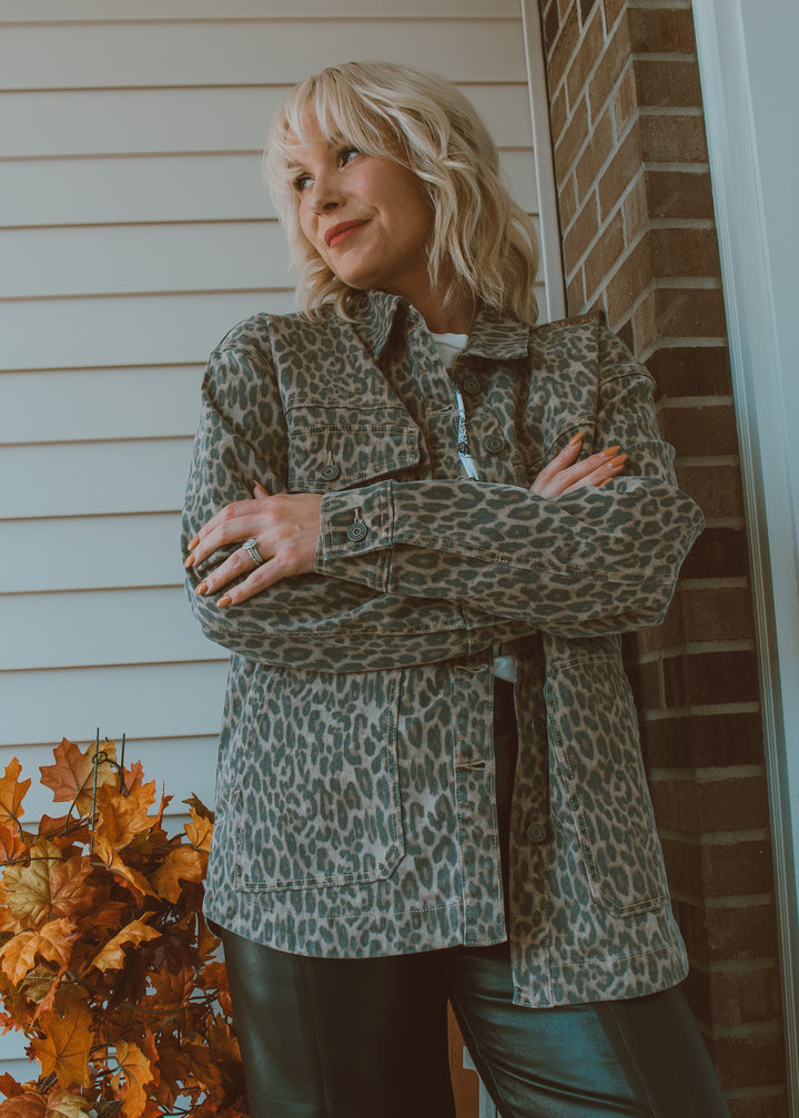 Woman wearing a leopard print jacket standing in front of a brick wall.