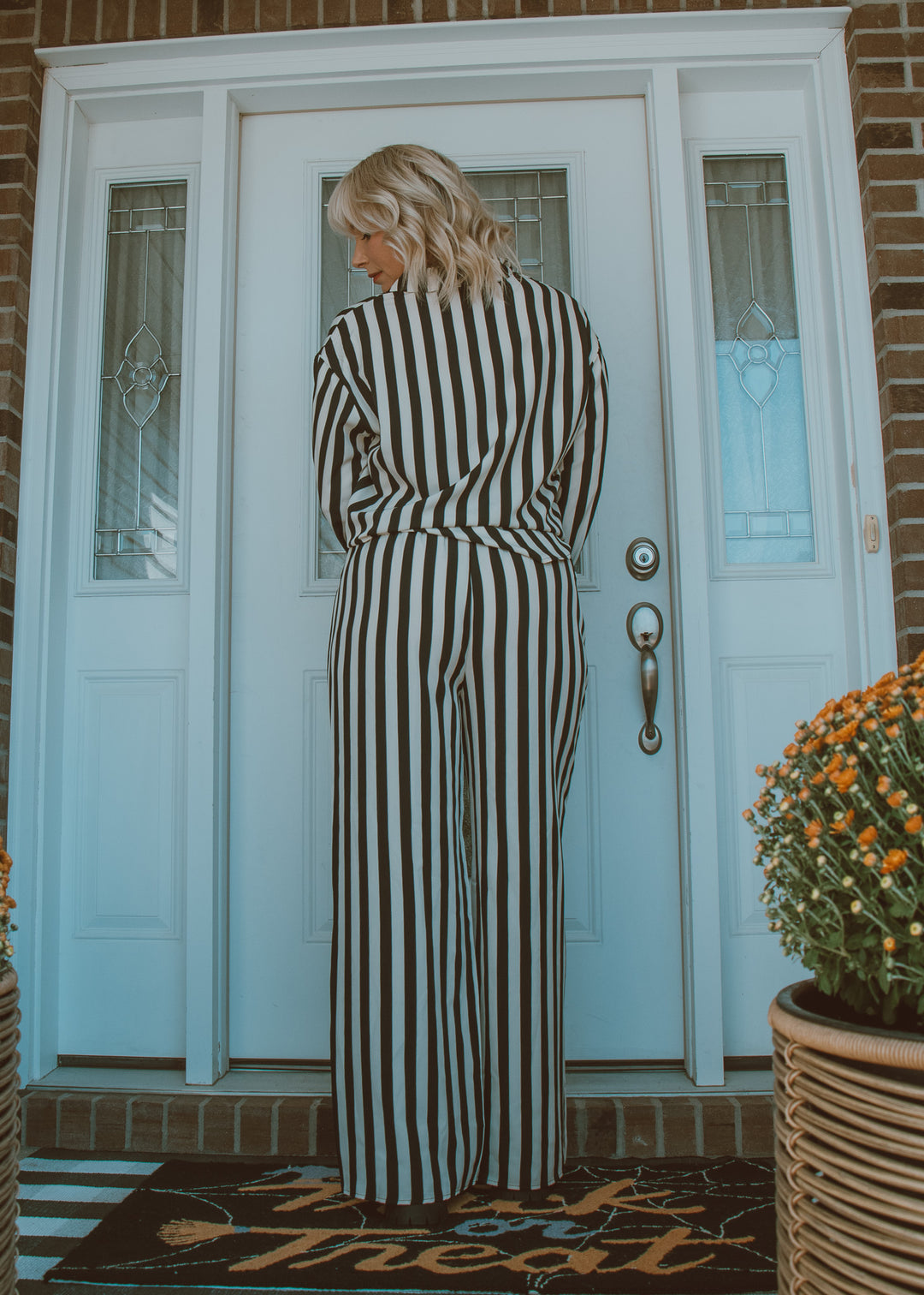 Person wearing a black and white striped outfit standing in front of a white door with glass panels.