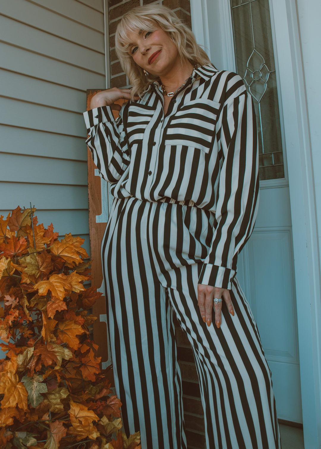 Person wearing a black and white striped outfit standing outside a house with autumn leaves.