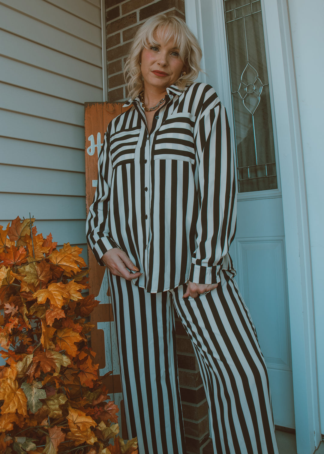 Person wearing a black and white striped outfit standing in front of a door with autumn leaves.
