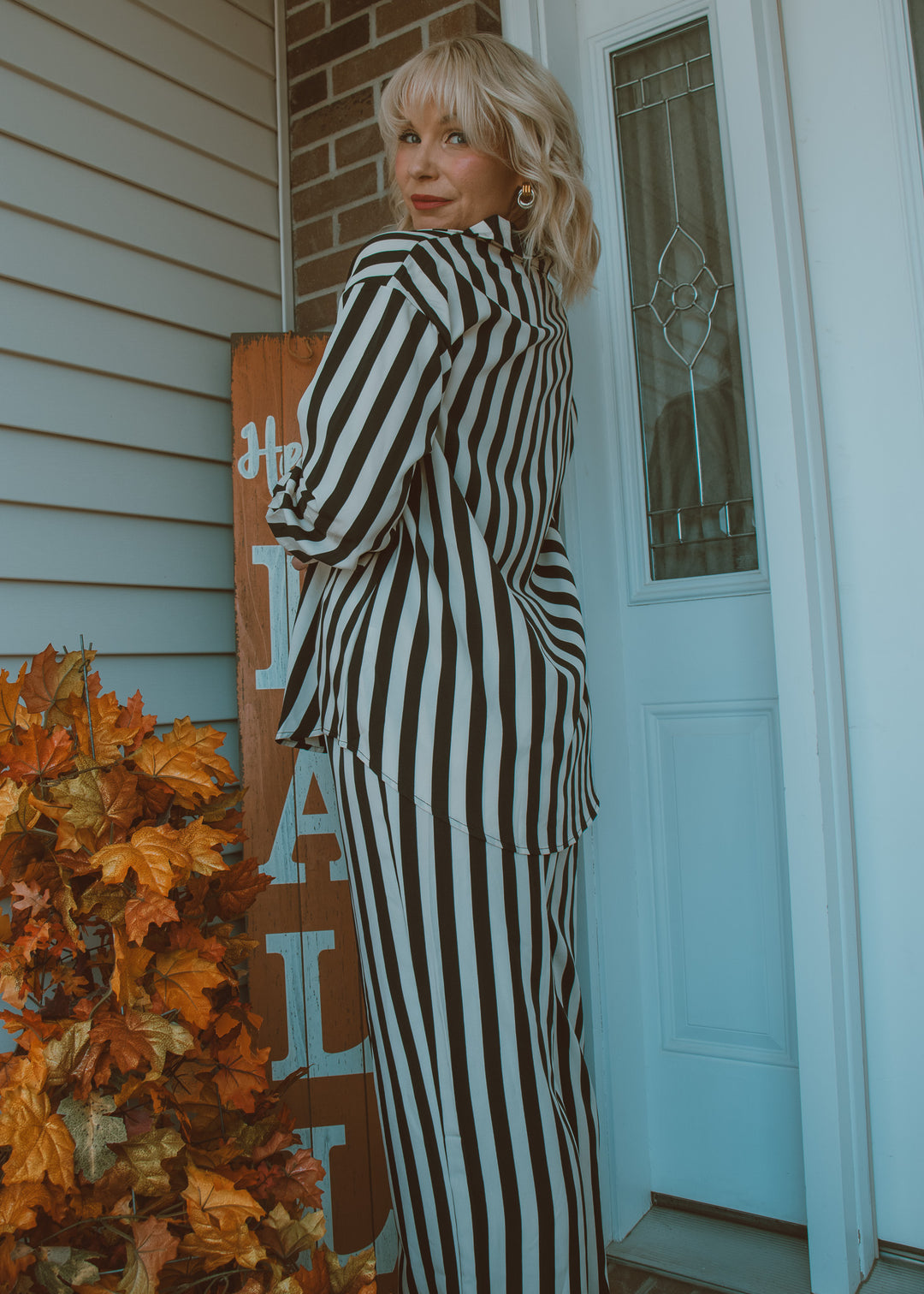 Woman in a black and white striped outfit standing on a porch with autumn decorations.