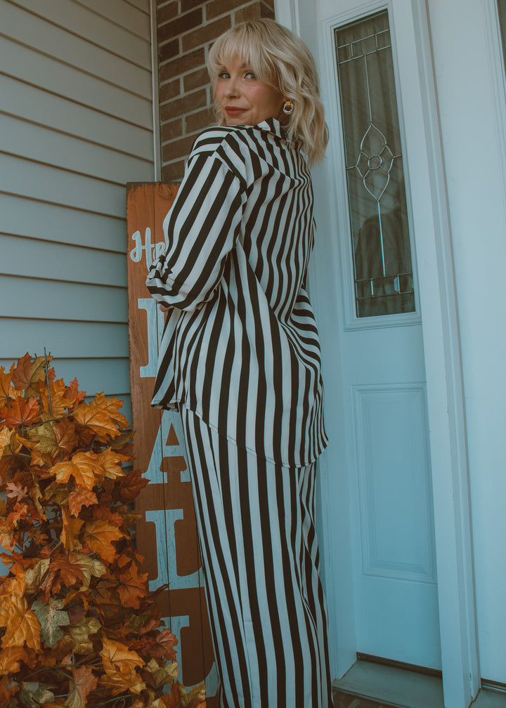 Woman in a black and white striped outfit standing on a porch with autumn decorations.