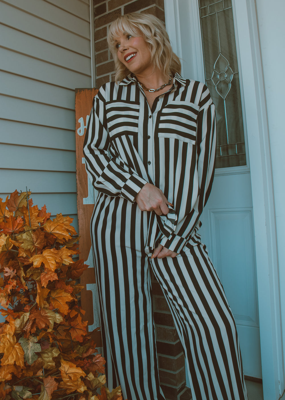 Woman in a black and white striped outfit standing outside a house with autumn leaves.