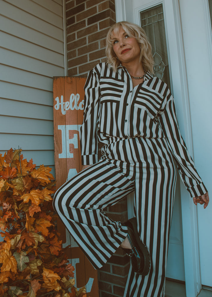 Person wearing a black and white striped outfit sitting on a step with autumn decorations.