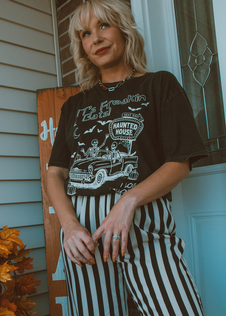 Person wearing a black graphic t-shirt with a car design and striped pants, standing in front of a door.