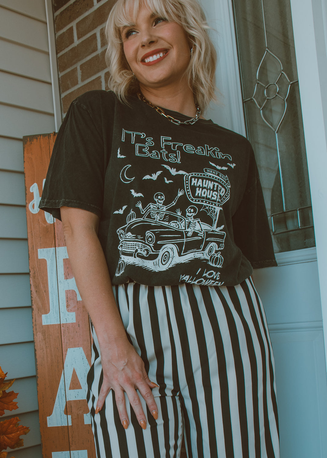 Woman wearing a graphic t-shirt with text and vintage car design, standing in front of a door.