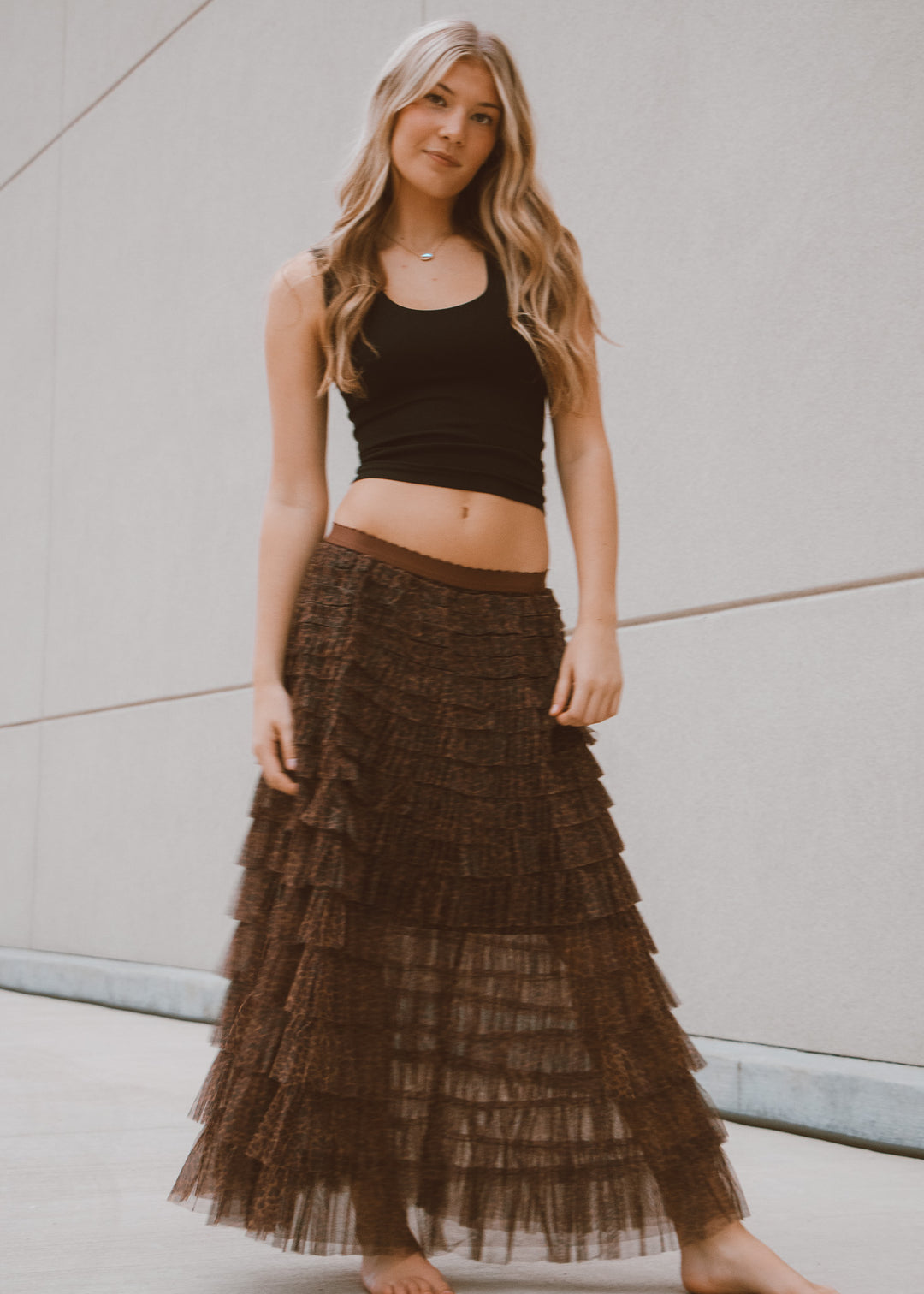 Woman wearing a black tank top and tiered brown skirt against a neutral background