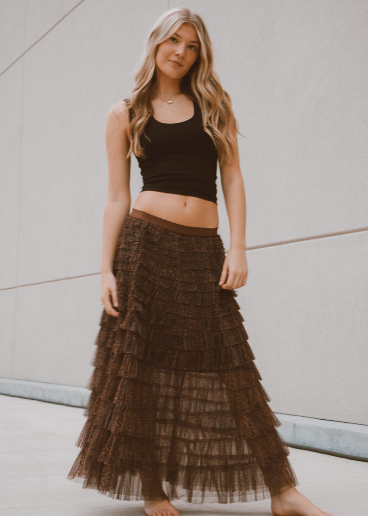 Woman wearing a black tank top and tiered brown skirt against a neutral background