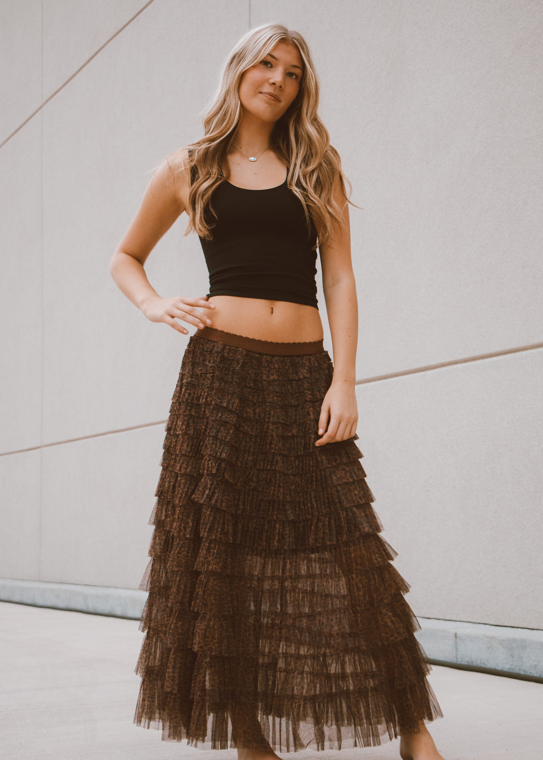 Woman wearing a black crop top and tiered brown skirt against a neutral background